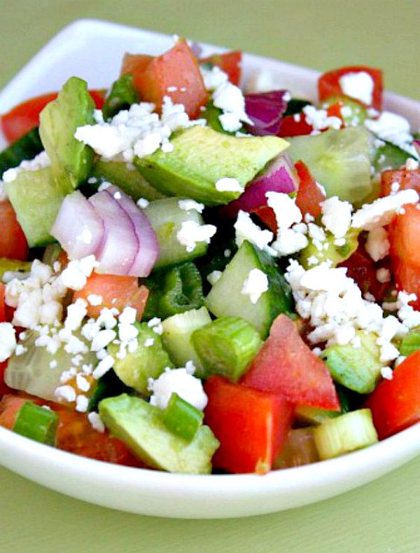 avocado cucumber tomato salad in a white bowl with a light green background