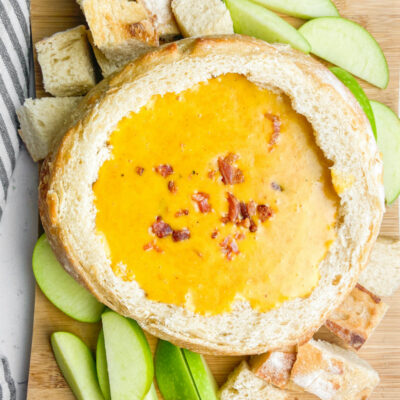 Cheddar Beer Fondue in a bread bowl with apples and bread chunks surrounding