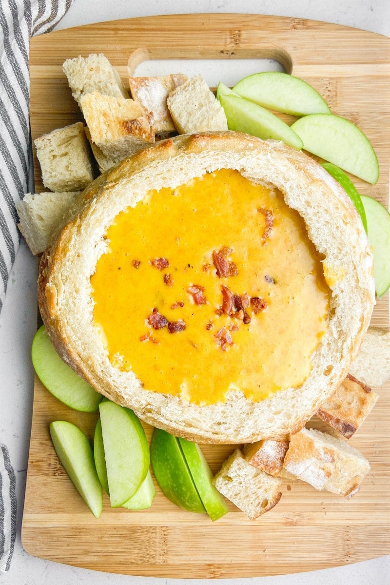 Cheddar Beer Fondue in a bread bowl with apples and bread chunks surrounding