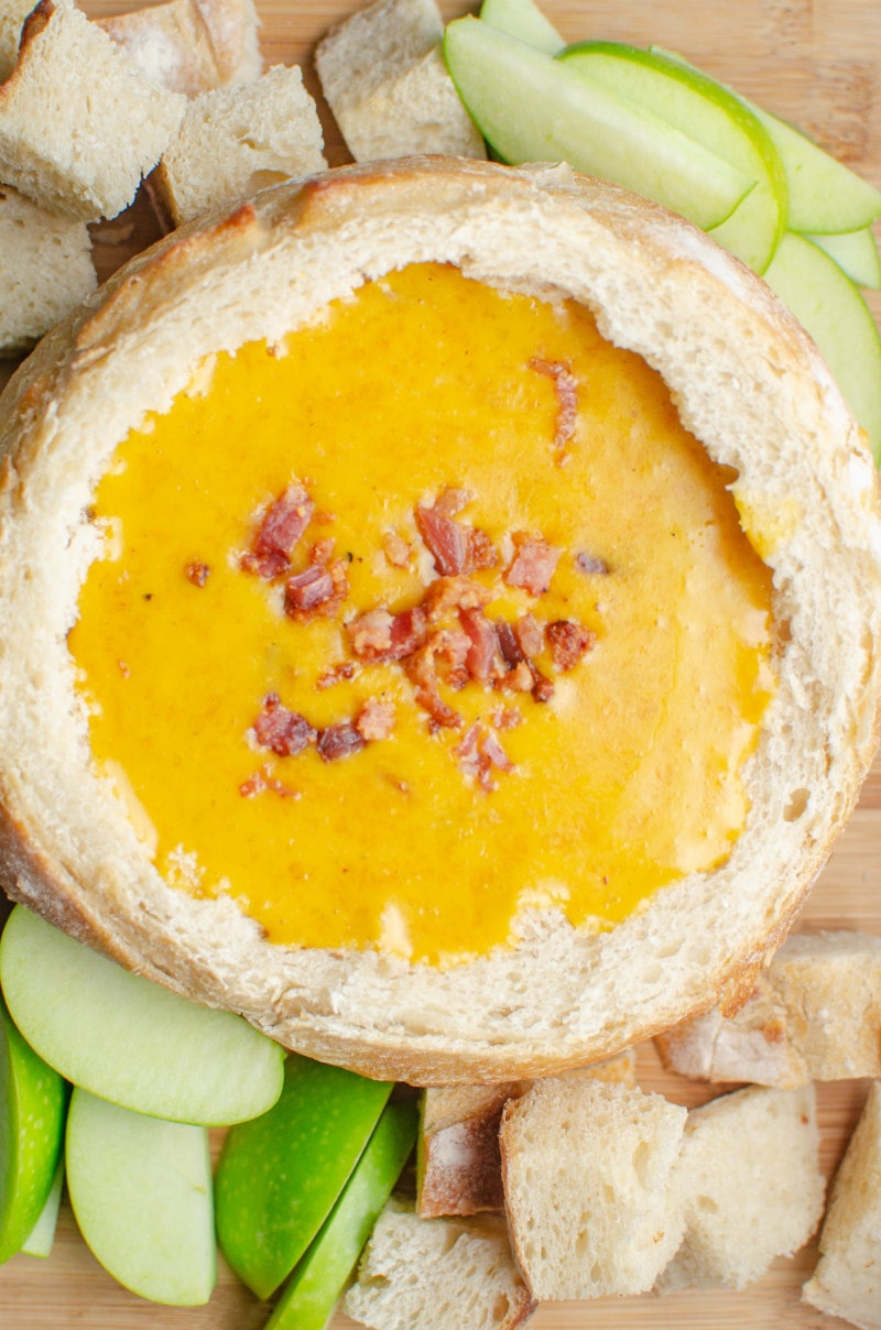 Cheddar Beer Fondue in a bread bowl with apples and bread chunks surrounding