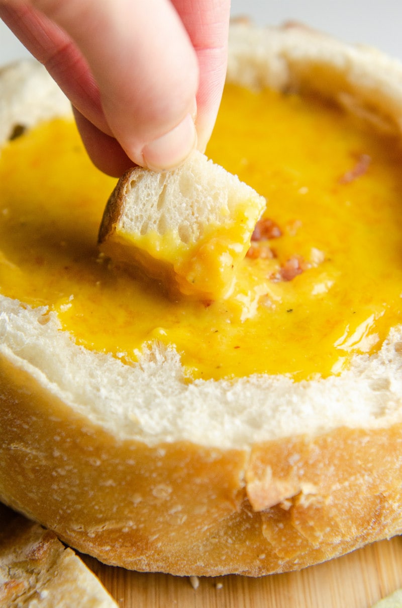 cheddar beer fondue hand dunking bread chunk into fondue