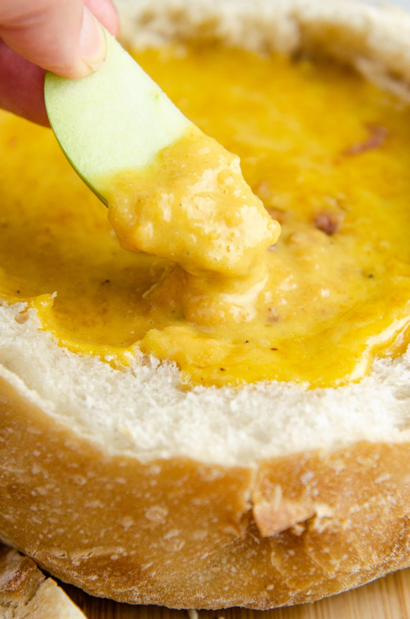 hand dunking apple slice into cheddar beer fondue