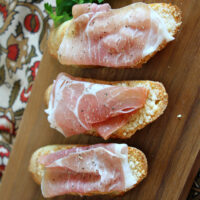 cheese crostini with prosciutto on serving board