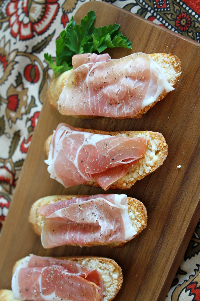 cheese crostini with prosciutto on serving board