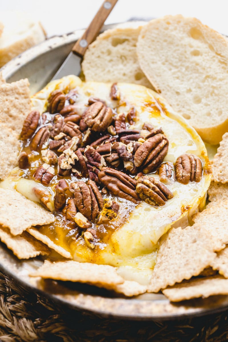 melted brie cheese with pecans surrounded by sliced baguette and crackers