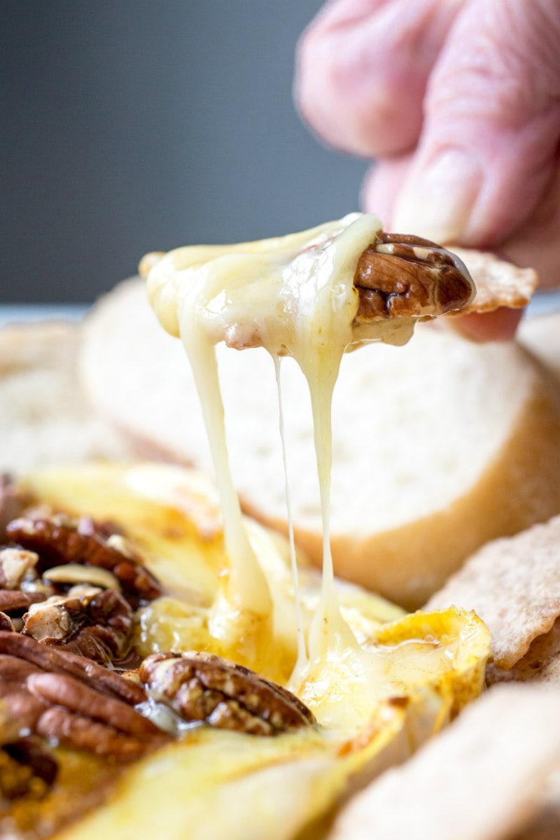 hand dipping baguette in melted brie cheese and pecans