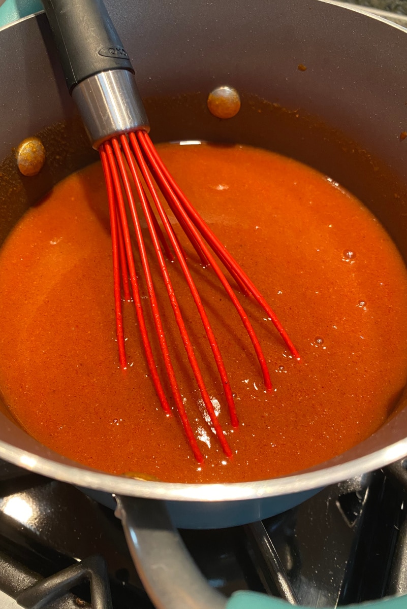 Best Enchilada Sauce recipe from RecipeGirl.com #best #enchilada #sauce #recipe #RecipeGirl #homemade making enchilada sauce in pan stirring with red whisk