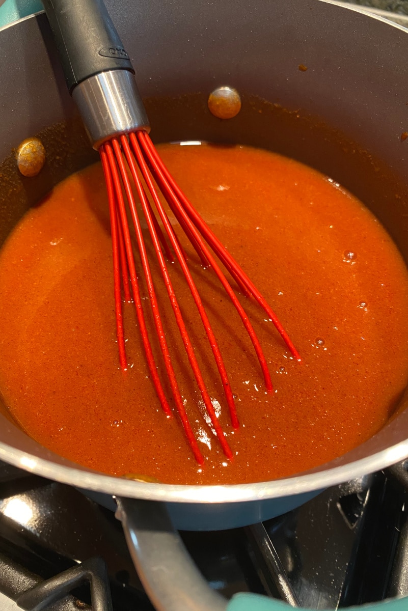 making enchilada sauce in pan stirring with red whisk