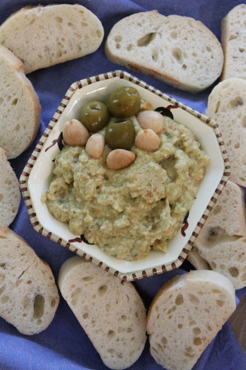 Green Olive and Almond Spread recipe from RecipeGirl.com #green #olive #greenolives #olives #almond #almonds #appetizer #spread #dip #recipe #RecipeGirl overhead shot of dish of green olive spread surrounded by baguette slices