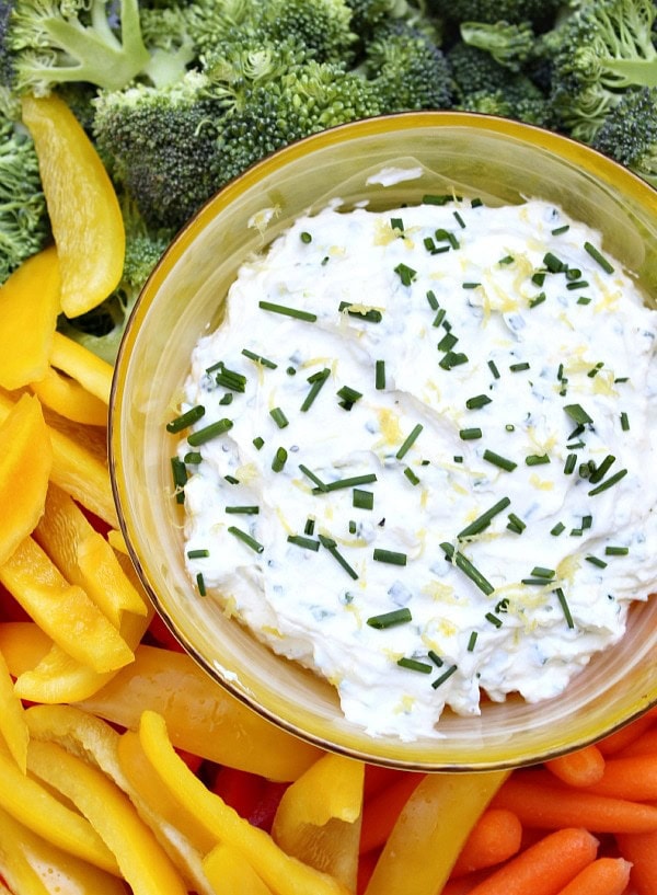 overhead shot of lemon chive cheese dip in a yellow bowl surrounded by yellow peppers, broccoli and carrots