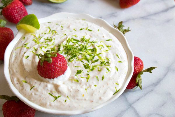 margarita fruit dip in a white bowl on a marble surface, garnished with strawberries and lime zest