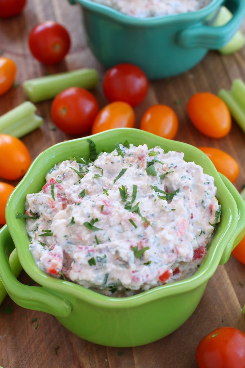 pine nut and feta cheese dip in a green dish surrounded by veggies