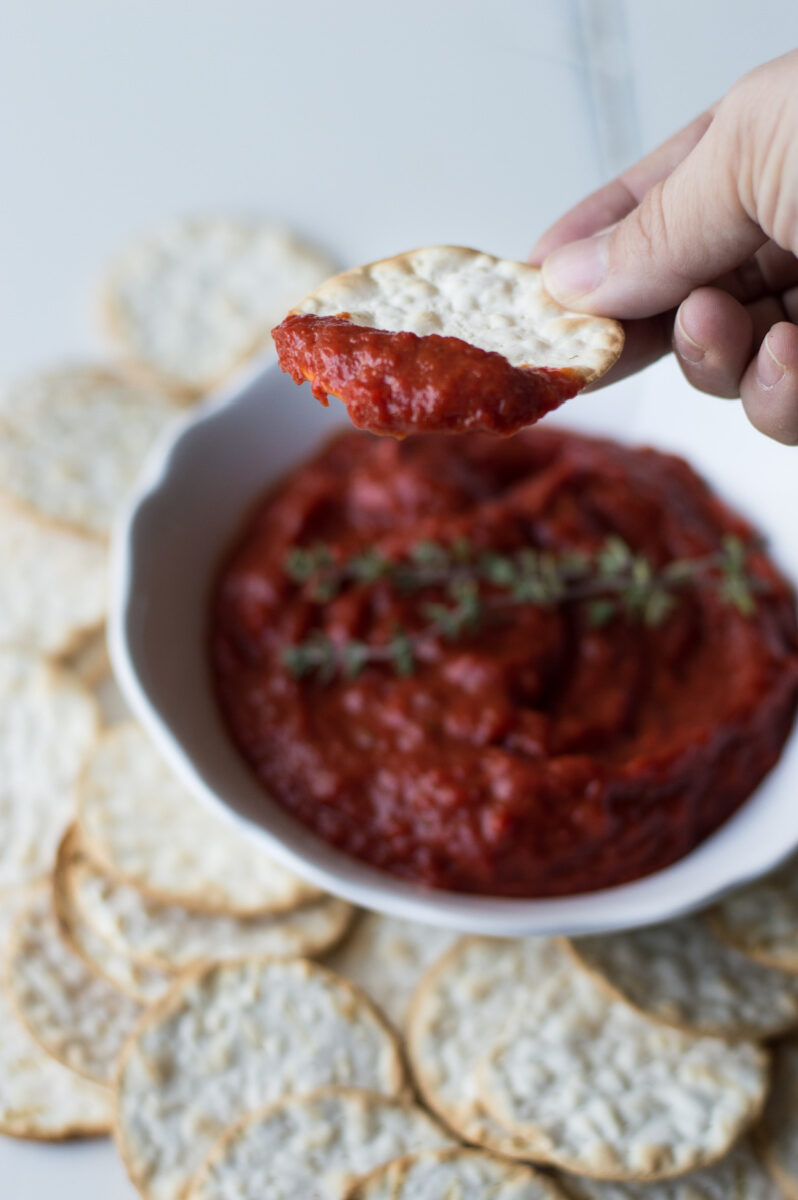 cracker dipping into red pepper spread