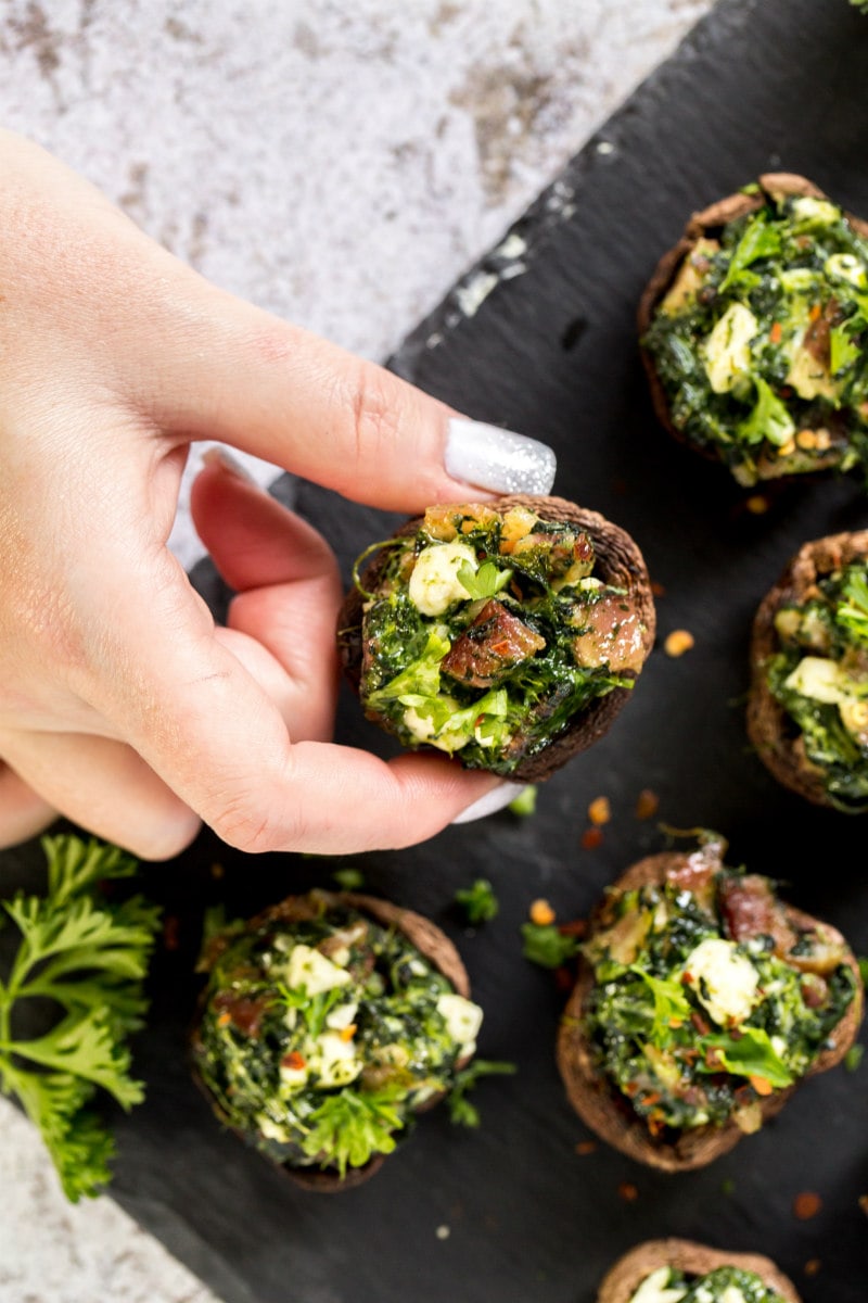 Roasted Mushrooms stuffed with feta, spinach and bacon recipe from RecipeGirl.com #roasted #stuffed #mushrooms #feta #spinach #bacon #recipe #RecipeGirl picking up a stuffed mushroom