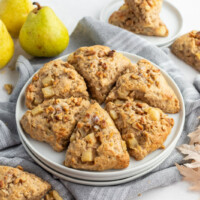 maple nut and pear scones on a white plate with fresh green pears in background