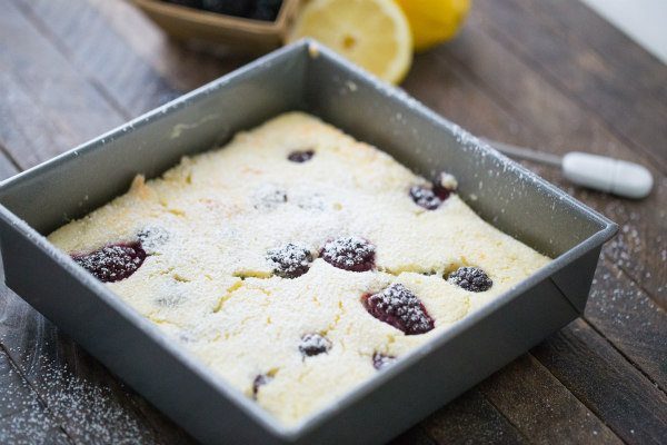 Blackberry Lemon Pudding Cake in a metal square pan with fresh lemon in the background