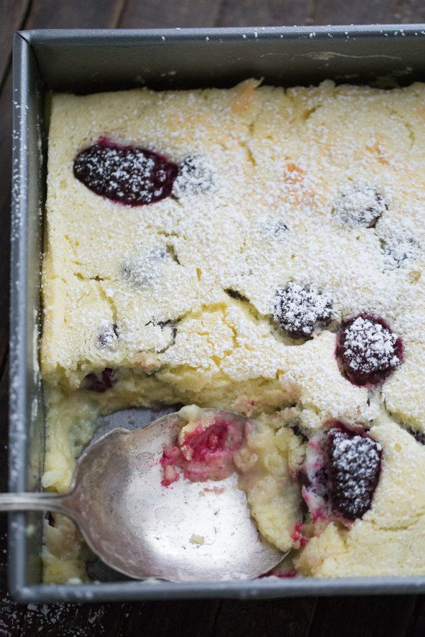 Blackberry Lemon Pudding Cake in a metal cake pan with a serving spoon taking some of the cake out of the pan