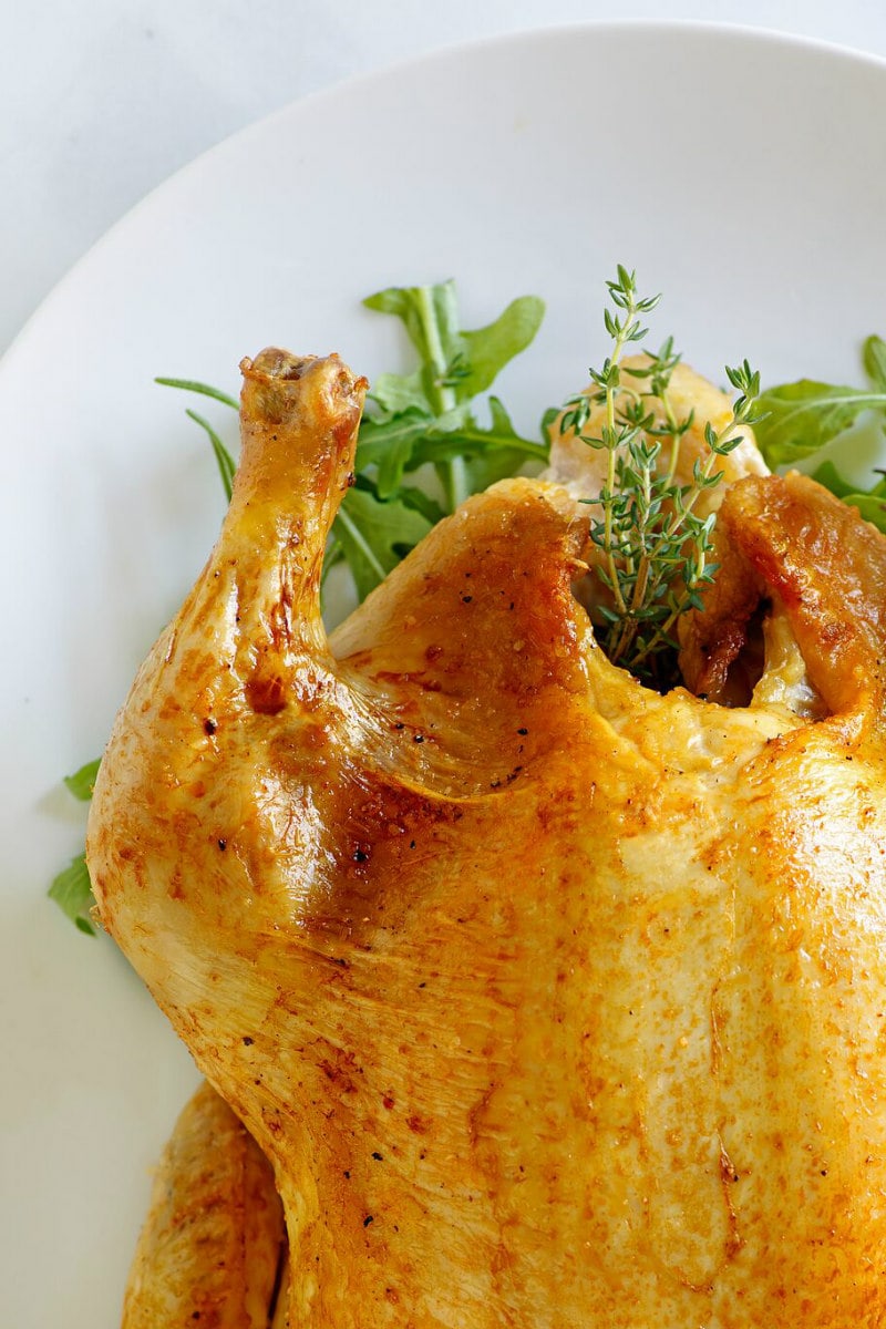 Cider Roasted Chicken recipe from RecipeGirl.com #cider #roasted #roast #chicken #fall #dinner #recipe #RecipeGirl peek at corner of Cider Roasted Chicken on white platter