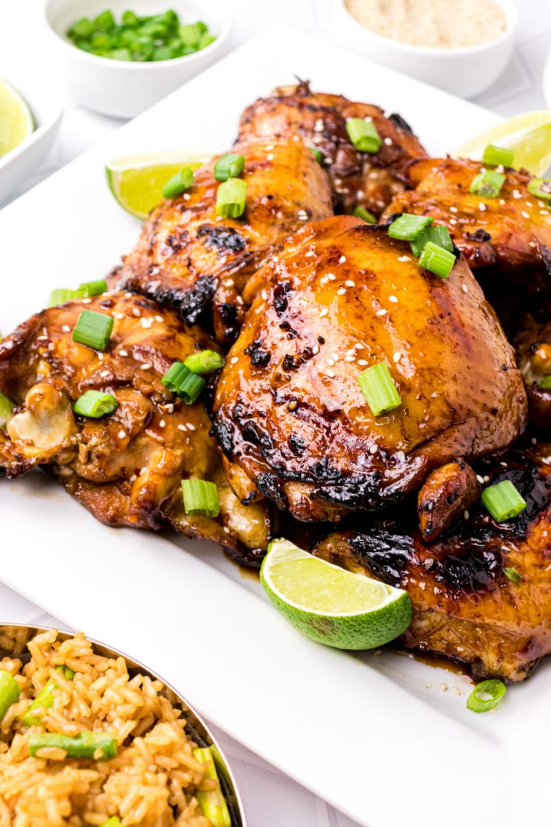 asian barbecue chicken on a white platter with chives and lime