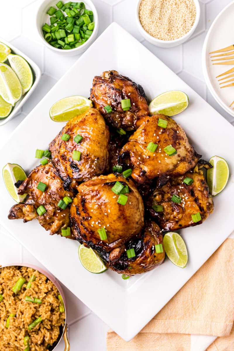 asian barbecue chicken on a white platter with chives and lime