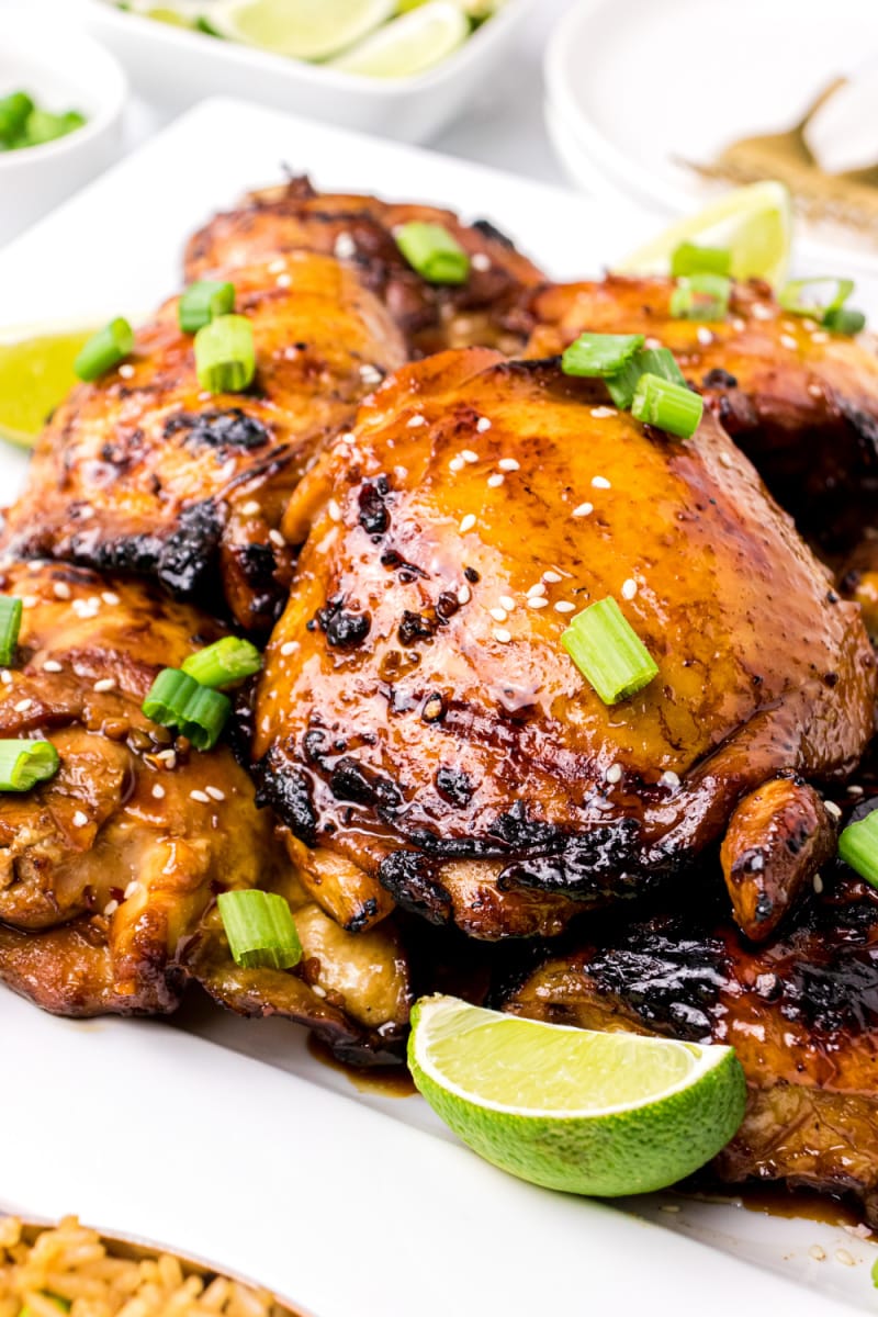 asian barbecue chicken on a white platter with chives and lime