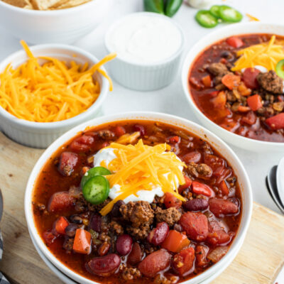 beef and bean chili in a white bowl topped with cheese and sour cream and jalapeno