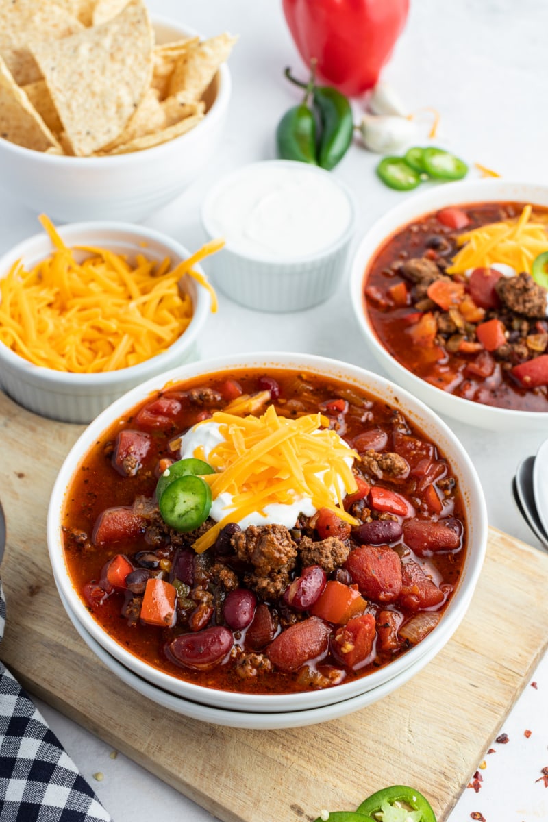 beef and bean chili in a white bowl topped with cheese and sour cream and jalapeno