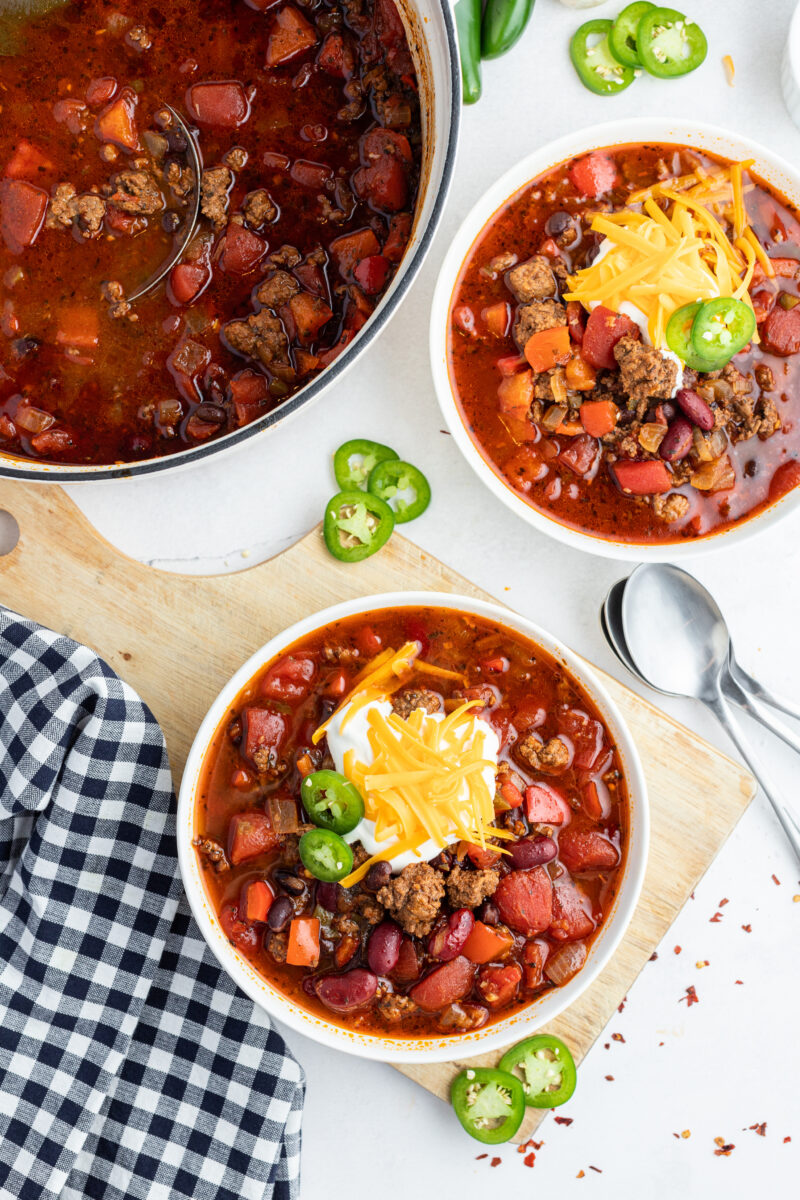 two bowls of beef and bean chili topped with cheese and sour cream and jalapeno