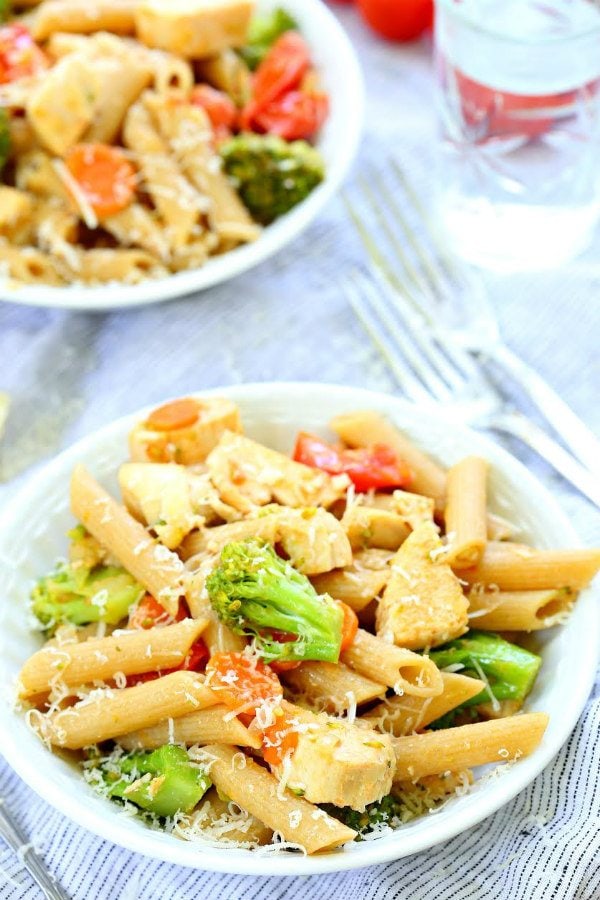 bowl of chicken pasta primavera in a white bowl with a fork on the side and another bowl of pasta in the background