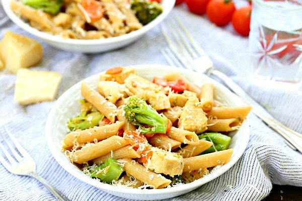 bowl of chicken pasta primavera in a white bowl with a fork on the side and another bowl of pasta in the background