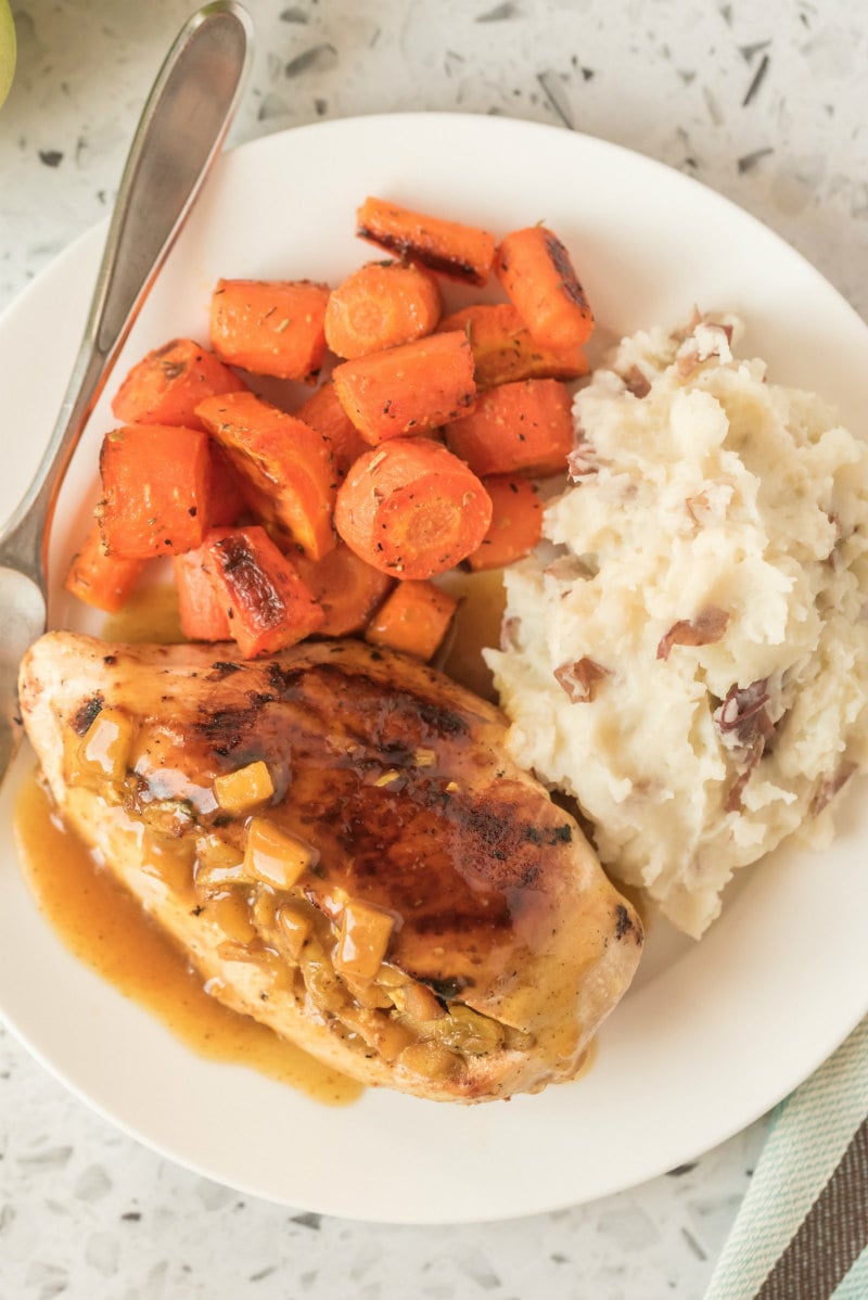 chicken with curried apple stuffing on a white plate with carrot and potato