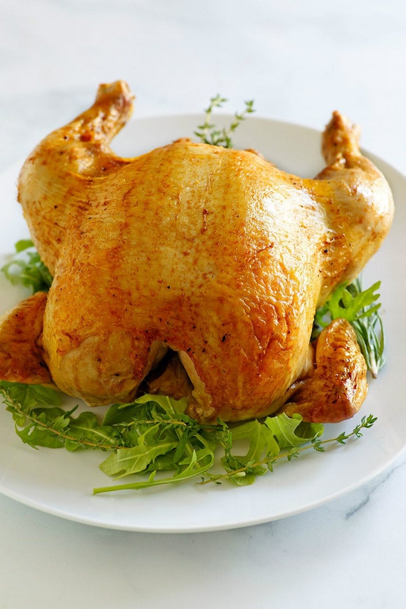 Cider Roasted Chicken recipe from RecipeGirl.com #cider #roasted #roast #chicken #fall #dinner #recipe #RecipeGirl Whole Cider Roasted Chicken on a platter with herb garnish