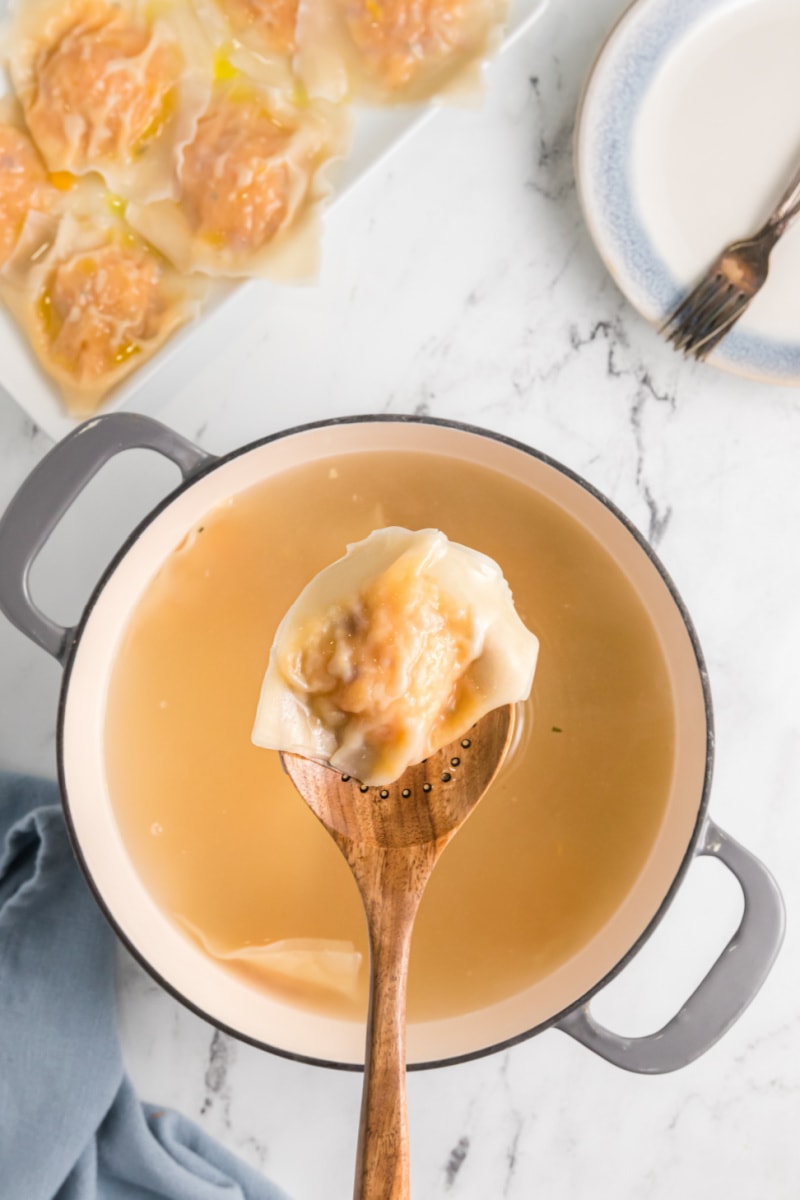 spoon holding ravioli above pot of water