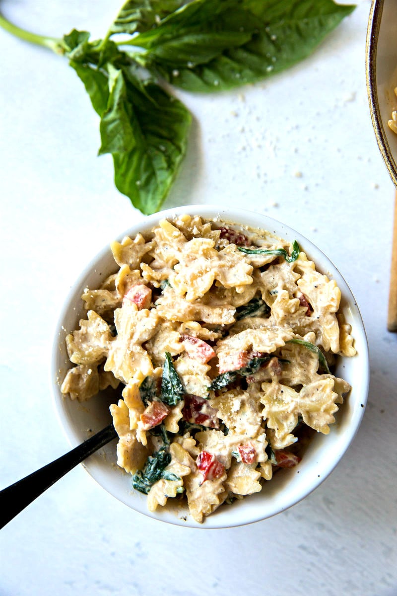 serving of farfalle pasta in a white bowl with a basil leaf on the side