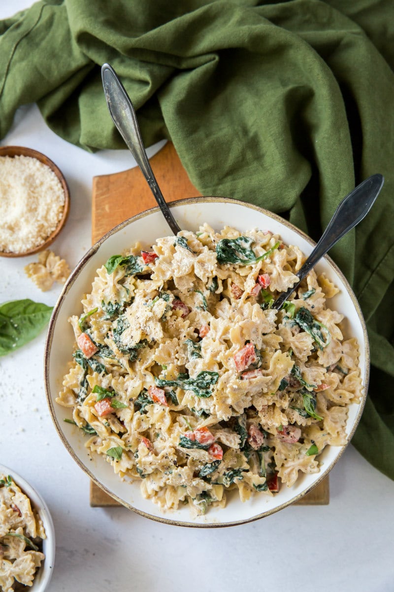 bowl of pasta with spinach and ricotta cheese with side of parmesan sitting on green napkin