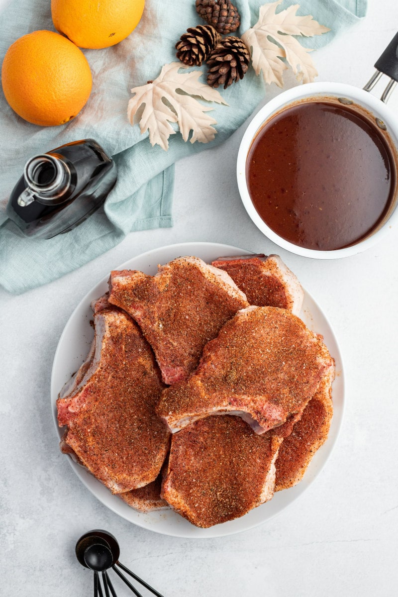 seasoned pork chops on white plate with bowl of maple cranberry glaze on the side