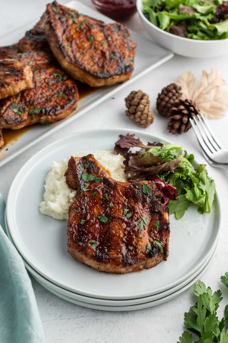 grilled pork chop on white plate with more pork chops on platter