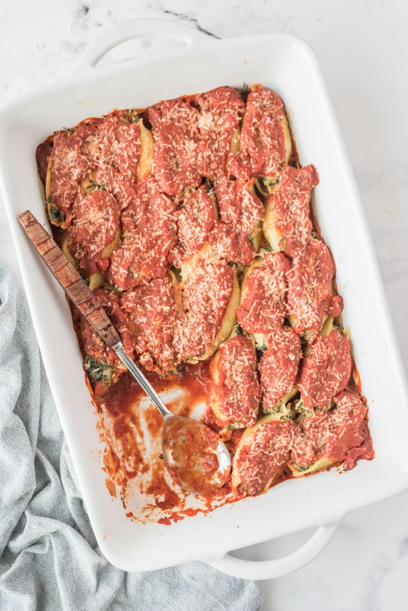 spooning stuffed shells out of a casserole dish