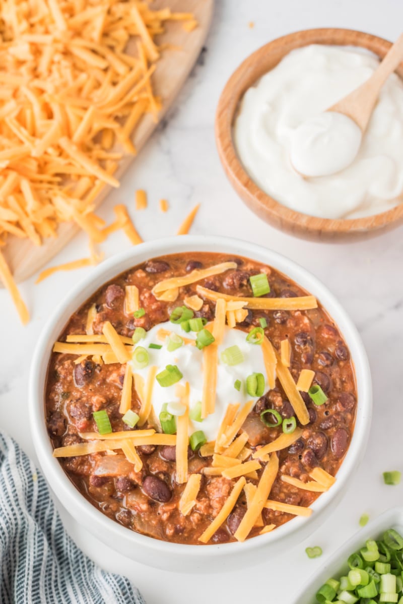 white bowl of mexican black bean and sausage chili with cheese and sour cream garnish