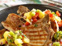 Grilled Pork Chops with tropical salsa on top set on a black dinner plate and a flowered napkin in the background