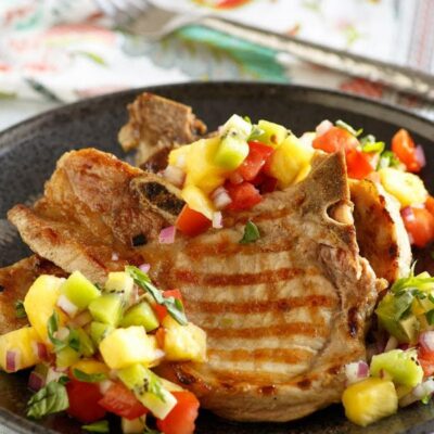 Grilled Pork Chops with tropical salsa on top set on a black dinner plate and a flowered napkin in the background