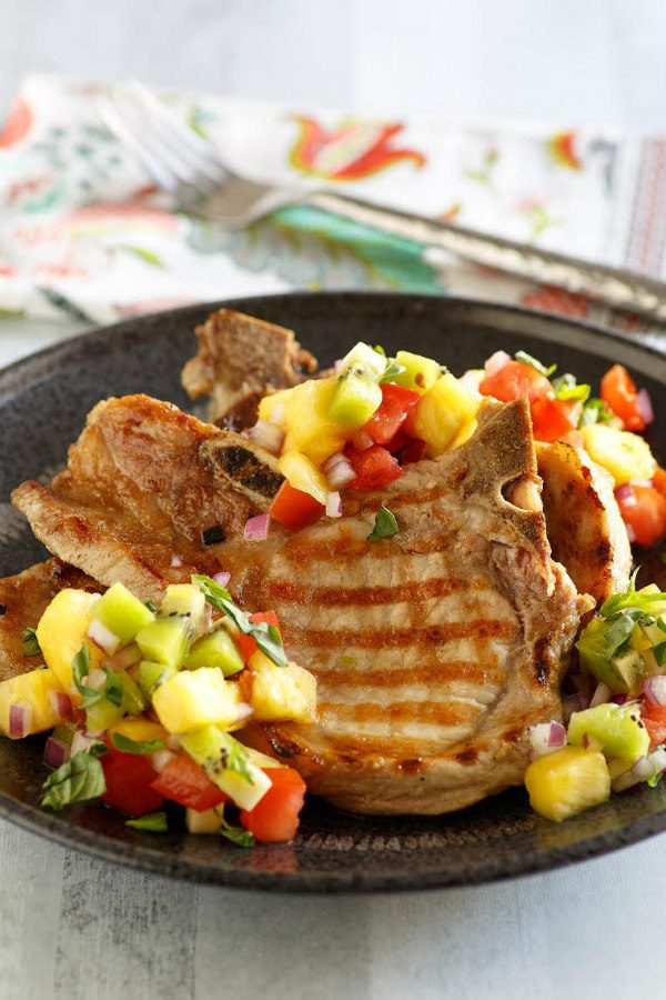 Grilled Pork Chops with Tropical Salsa set on a black plate with a fork on a flowered napkin in the background