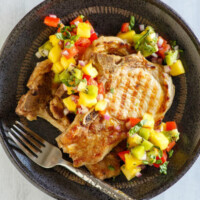 overhead shot of grilled pork chops with tropical salsa on a black plate with a fork