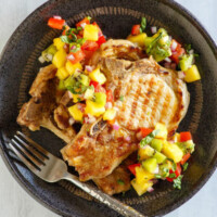 overhead shot of grilled pork chops with tropical salsa on a black plate with a fork