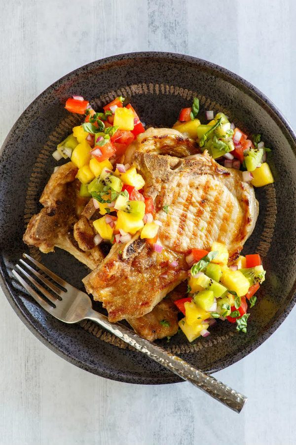 Overhead shot of Grilled Pork Chops with Tropical Salsa on a black plate with a fork