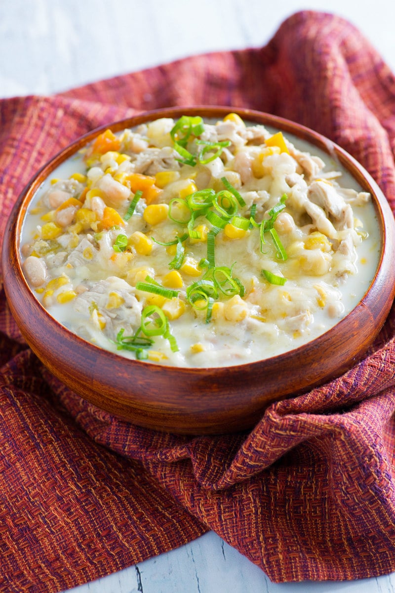 Bowl of White Chicken Chili in an orange bowl set on a orange/red patterned cloth napkin