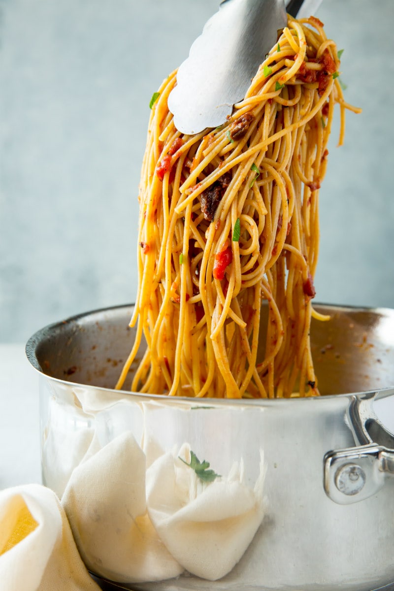 Spaghetti with Three Tomato Sauce recipe from RecipeGirl.com #spaghetti #pasta #three #tomato #sauce #sundriedtomatoes #sundried #tomatoes #cherrytomatoes #cherry #tomatoes #recipe #RecipeGirl tongs pullling spaghetti with 3 tomato sauce out of a silver pot