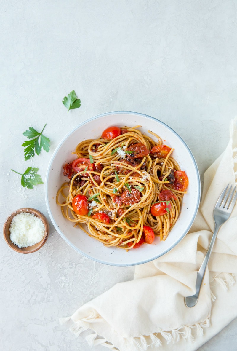 Spaghetti with Three Tomato Sauce recipe from RecipeGirl.com #spaghetti #pasta #three #tomato #sauce #sundriedtomatoes #sundried #tomatoes #cherrytomatoes #cherry #tomatoes #recipe #RecipeGirl spaghetti with three tomato sauce in a white bowl with a napkin and fork on the side. bowl of salt and fresh parsley in view too