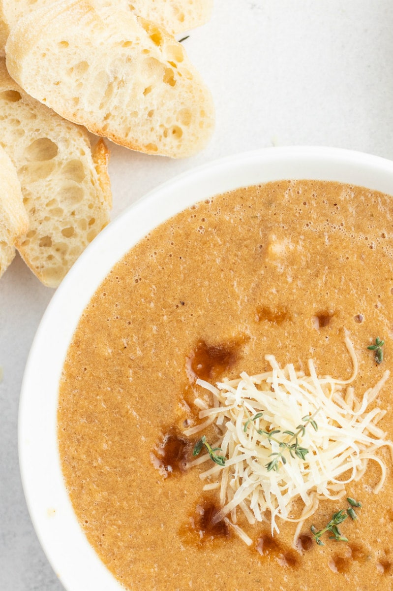 close up peek of caramelized onion soup in a white bowl bread on side