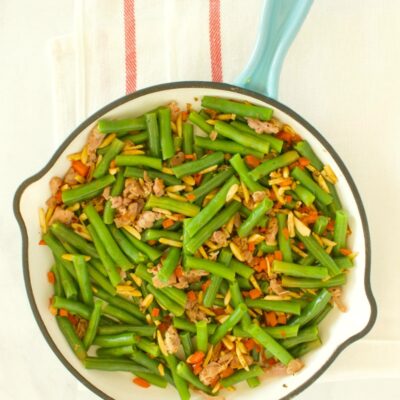 overhead shot of green beans with prosciutto in a fry pan with a blue handle, set on a yellow napkin with red stripes